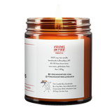 Back label of amber glass candle jar showing product details for Virgins On Fire Candle Co, a funny candle, gay-owned small business in Brooklyn, NY. 100% soy wax, handmade in Brooklyn, 45-50 hour burn time, non-toxic, 9oz size. Features Virgins on Fire Candle Co. branding, contact information, and cartoon flame mascot with rainbow flag. Includes a note about being handmade by a gay man rather than a corporation with a rainbow logo 30 days out of the year."