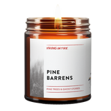 Handcrafted amber jar candle from queer-owned Virgins on Fire Candle Co. featuring 'Pine Barrens' scent with pine trees and ghost stories theme. White label with misty forest imagery and pride flag logo.
