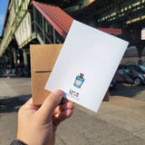 back of the pizza rat card. maker is holding it outside hte subway. the card has a photo of a rat in a coffee cup on it.