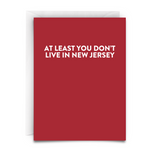 a red greeting card with white font that says "At Least You Don't Live in New Jersey." White Envelope Included.