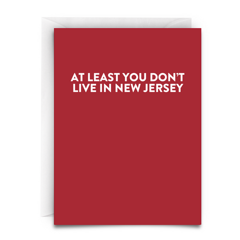 a red greeting card with white font that says "At Least You Don't Live in New Jersey." White Envelope Included.