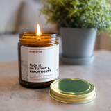 fuck it i'm buying a beach house candle on a table with a plant in background.