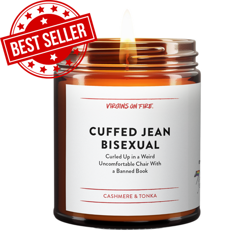 Best-selling amber glass funny candle from Virgins On Fire Candle Co., a gay-owned Brooklyn, NY small business. Label reads 'Cuffed Jean Bisexual' with subtitle 'Curled Up in a Weird Uncomfortable Chair With a Banned Book.' Cashmere and tonka scent. Features red bestseller stamp.