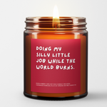 Candle called Doing My Silly Little Job While The World Burns. Red Background. White Font. Lit.