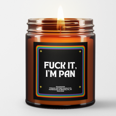 Candle in an amber jar with a label that says "fuck it, I'm pan" - the label has a rainbow border. There are candle details - like that it's teakwood scented and 9oz.
