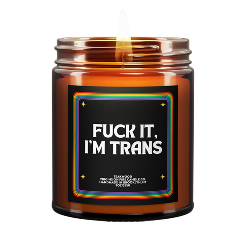 LGBTQ+ pride-themed candle in amber glass jar from Brooklyn-based Virgins on Fire, featuring bold text with rainbow border design. Handmade teakwood scented candle with inclusive messaging and pride flag emblem.