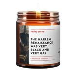 Amber glass candle jar with white label featuring vintage jazz musician photo. Label reads 'The Harlem Renaissance Was Very Black and Very Gay' with Cardamom & Cream scent description. Small pride flag icon visible. Made by Virgins on Fire company.