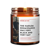 Amber glass candle jar with white label featuring vintage jazz musician photo. Label reads 'The Harlem Renaissance Was Very Black and Very Gay' with Cardamom & Cream scent description. Small pride flag icon visible. Made by Virgins on Fire company.