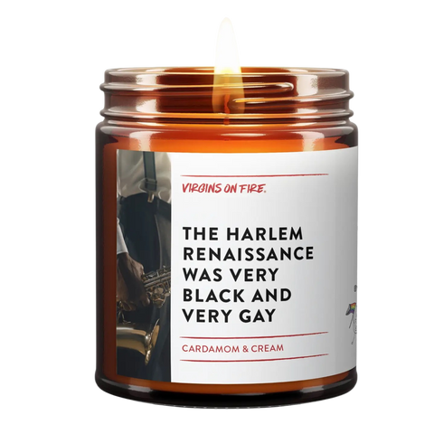 Amber glass candle jar with white label featuring vintage jazz musician photo. Label reads 'The Harlem Renaissance Was Very Black and Very Gay' with Cardamom & Cream scent description. Small pride flag icon visible. Made by Virgins on Fire company.