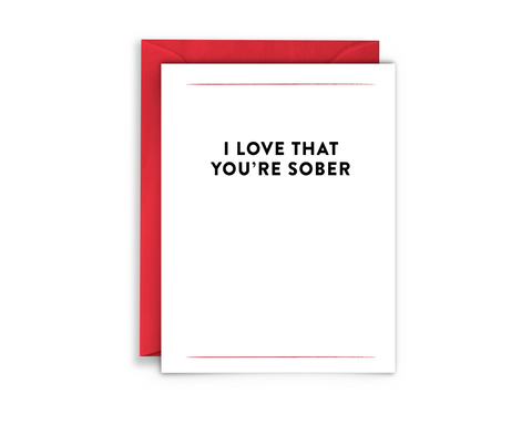 red envelope, white background greeting card with black text that reads, "I love that you're sober" in bold lettering. this is a message of sobriety support from virgins on fire candle co - a sober run business.