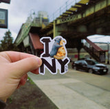 A photo outside of a subway station of someone holding a I Pizza Rat NY Sticker