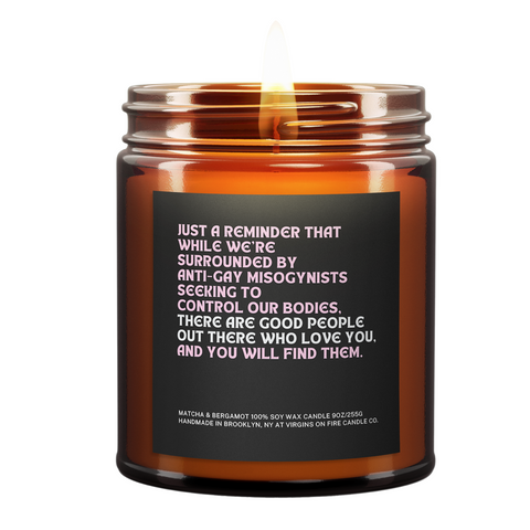 Inspirational LGBTQ+ solidarity candle from queer-owned Virgins On Fire Candle Co. in Brooklyn. Features empowering message of hope and community on black label with pink text. Matcha & Bergamot scented 9oz soy wax candle in amber glass jar. Handmade with pride and purpose, combining activism with aromatherapy.