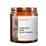 Amber glass candle from Virgins On Fire Candle Co., a funny gay-owned Brooklyn, NY candle business. Label reads 'Lesbians and Taco Trucks' with mint mojito scent. Features black and white lifestyle photographs and lit wick. Small pride flag icon visible.