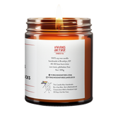Back label of amber glass candle jar showing product details for Virgins On Fire Candle Co, a funny candle, gay-owned small business in Brooklyn, NY. 100% soy wax, handmade in Brooklyn, 45-50 hour burn time, non-toxic, 9oz size. Features Virgins on Fire Candle Co. branding, contact information, and cartoon mascot with rainbow flag. Includes a note about being handmade by a gay man rather than a corporation with a rainbow logo 30 days out of the year."