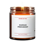 an amber jar candle that reads, "Madam President" it is dry gin and cypres scented. lit candle.