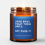 lit amber jar candle. blue background. it says, "some boys paint their nails, get over it." white eucalyptus scented.