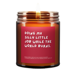Candle called Doing My Silly Little Job While The World Burns. Red Background. White Font. Lit.