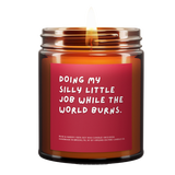 Candle called Doing My Silly Little Job While The World Burns. Red Background. White Font. Lit.