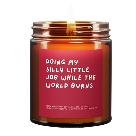 Candle called Doing My Silly Little Job While The World Burns. Red Background. White Font. Lit.