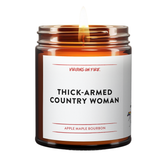 a brown amber jar candle with lit flame. the title in bold black font is Thick-Armed Country Woman. The scent below in red font is Apple Maple Bourbon. It is from Virgins On Fire Candle Company.