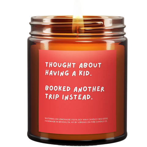 Amber candle. Burning. Says, "Thought about having a kid. Booked another trip instead." Read background. Fun White font.