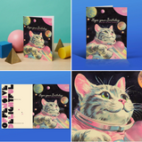 a cartoon cat - pink and gray - in a space suit floating in space around pastel colored planets. It says in script, "hope your birthday is out of this world." the back says that it's made by Offensive and Delightful - a card company.