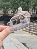 The maker holding it outside. A vintage style BODEGA CAT CASH REGISTER STICKER. A gray cat resting on an old bodega cash register with a sign that says Lost in the City.