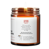 Back label of amber glass candle jar showing product details. 100% soy wax, handmade in Brooklyn, 45-50 hour burn time, non-toxic, 9oz size. Features Virgins on Fire Candle Co. branding, contact information, and cartoon mascot with rainbow flag. Includes note about being handmade by a gay man rather than a corporation with a rainbow logo 30 days out of the year."