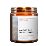 Amber glass candle jar from Virgins On Fire Candle Co., a gay-owned Brooklyn business. Label reads 'Among the Wildflowers' with floral bouquet scent. Features wildflower field imagery