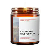 Amber glass candle jar from Virgins On Fire Candle Co., a gay-owned Brooklyn business. Label reads 'Among the Wildflowers' with floral bouquet scent. Features wildflower field imagery