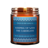 Winter-themed sweater style label. soy candle from Brooklyn's LGBTQ+-owned 'Virgins on Fire' featuring blue knit sweater pattern and text 'Keeping Up with the Cardigans', scented with Black Absinthe