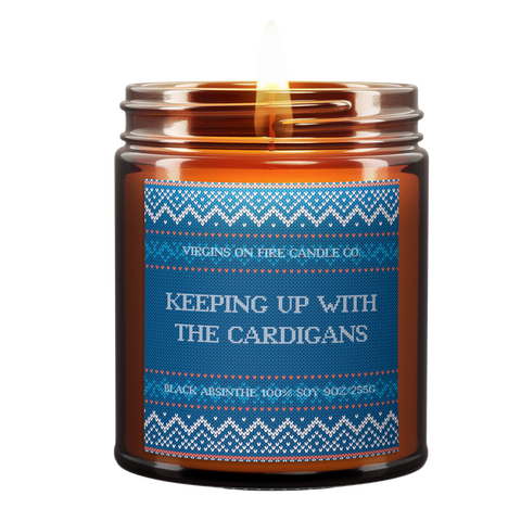Winter-themed sweater style label. soy candle from Brooklyn's LGBTQ+-owned 'Virgins on Fire' featuring blue knit sweater pattern and text 'Keeping Up with the Cardigans', scented with Black Absinthe