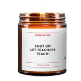 "Shut up let teachers teach" is a candle. this is a photo of it. lit. brown amber jar. it is tonka and oud scented.