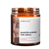 this is a brown amber jar candle with the text, "mansplaining the grill." it is a citronella candle. 