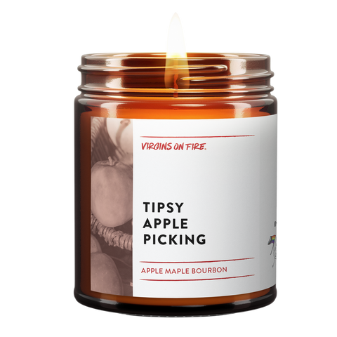 Virgins on Fire funny brand scented candle in amber glass jar, 'Tipsy Apple Picking' scent featuring apple maple bourbon fragrance. White label with vintage-style apple orchard photo background.